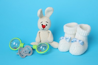 Photo of Baby rattle, pacifier, toy bunny and booties on light blue background