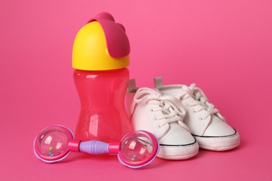 Photo of Baby rattle, bottle and booties on crimson background