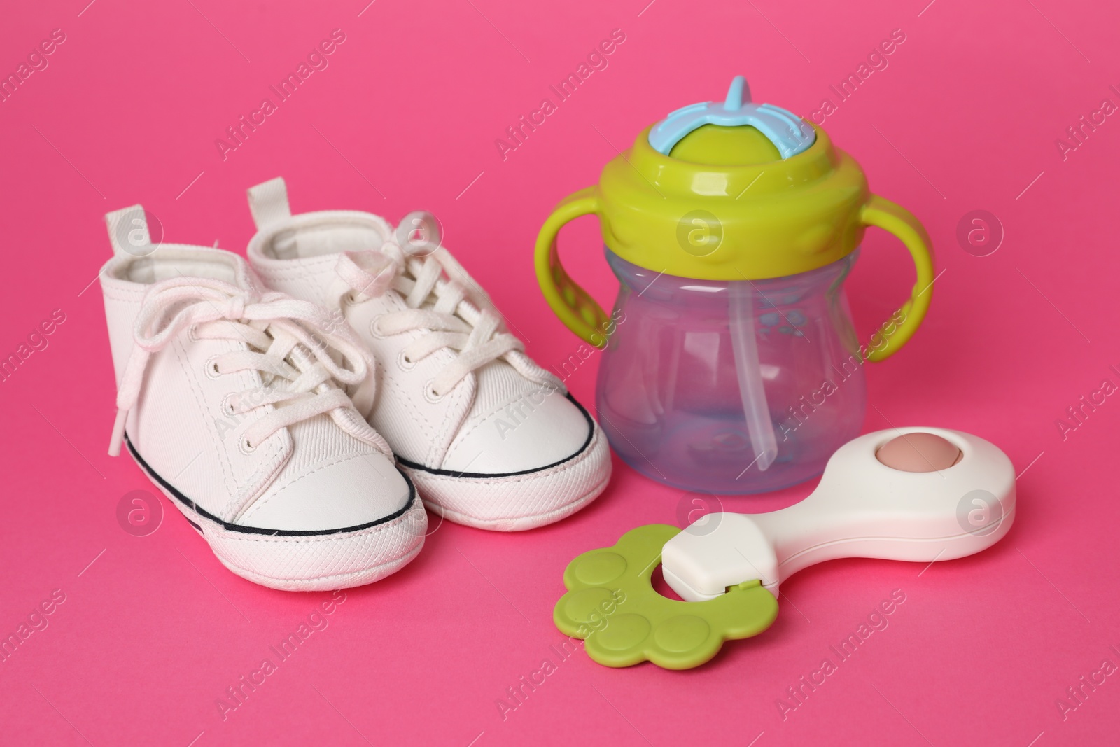 Photo of Baby rattle, bottle and booties on crimson background