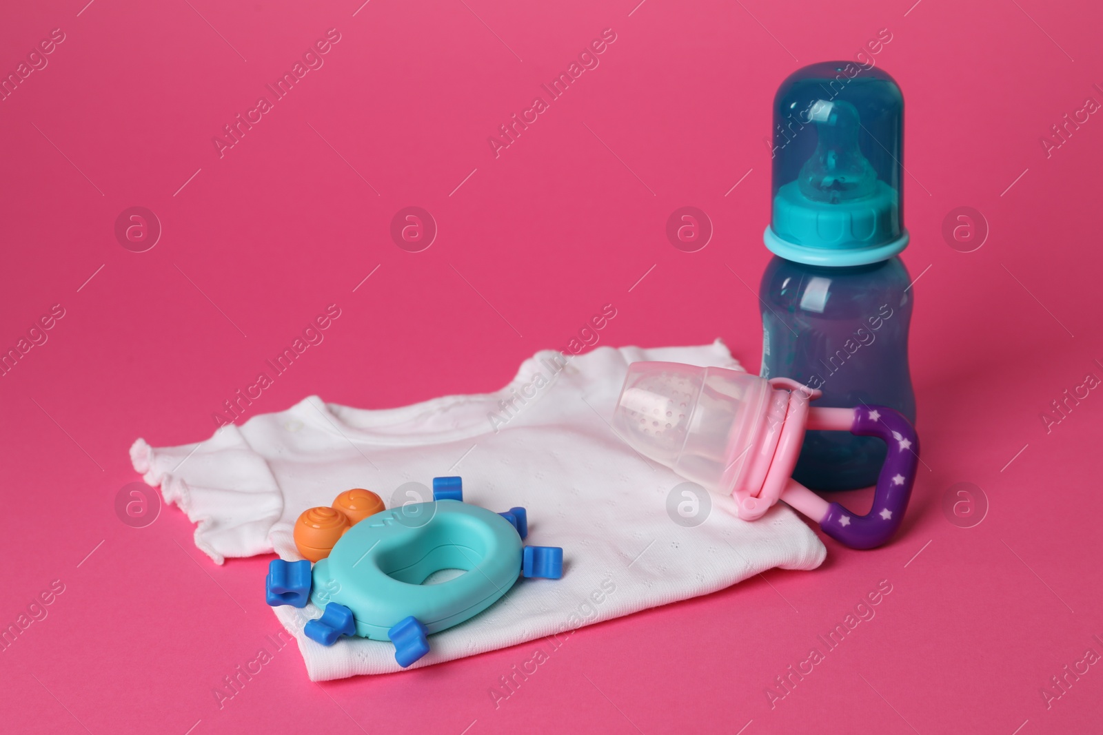 Photo of Baby rattle, body, bottle and nibbler on crimson background