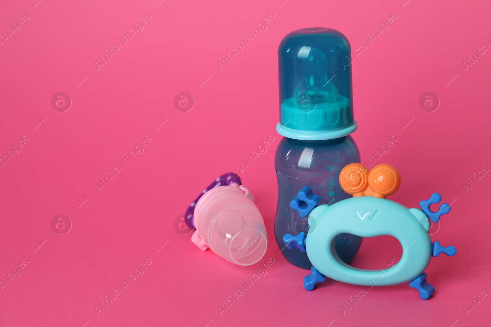 Photo of Baby rattle, bottle and nibbler on crimson background. Space for text