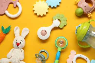 Different baby rattles on yellow background, flat lay