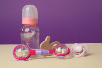 Photo of Baby rattles, pacifier and bottle on beige table. Space for text