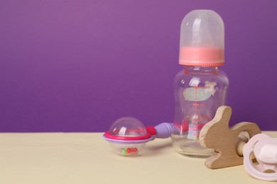 Baby rattles, pacifier and bottle on beige table. Space for text