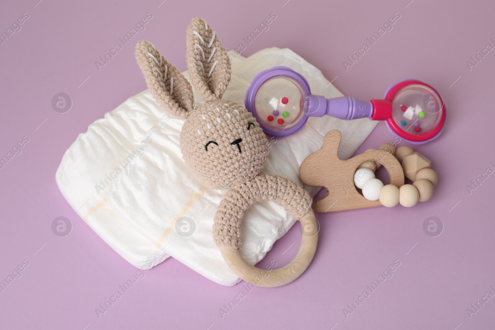 Photo of Baby rattles and diapers on lilac background