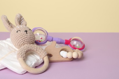 Photo of Baby rattles and diapers on lilac table, closeup. Space for text