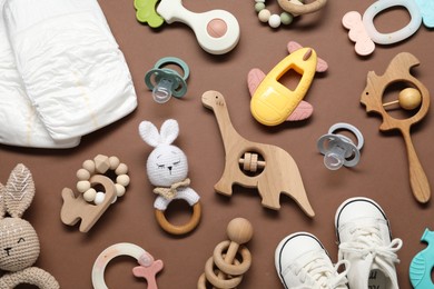 Photo of Different baby rattles and diapers on brown background, flat lay