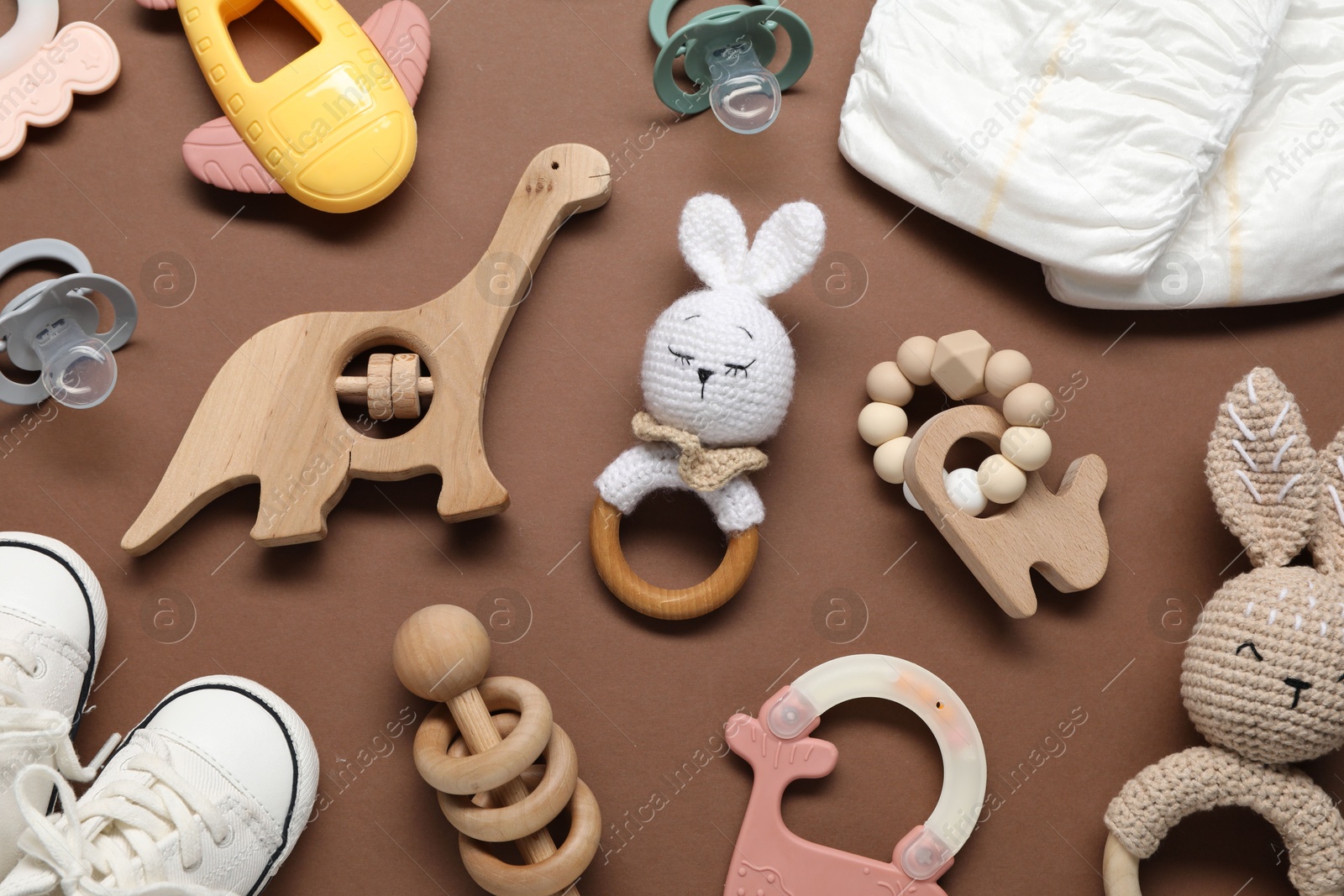 Photo of Different baby rattles and diapers on brown background, flat lay