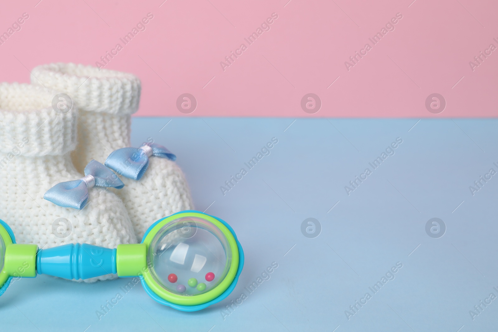 Photo of Baby rattle and booties on light blue table. Space for text