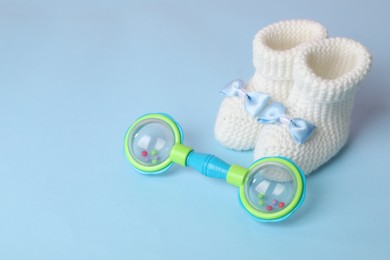 Photo of Baby rattle and booties on light blue background. Space for text