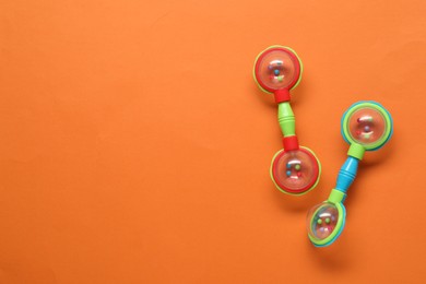 Colorful baby rattles on orange background, flat lay. Space for text