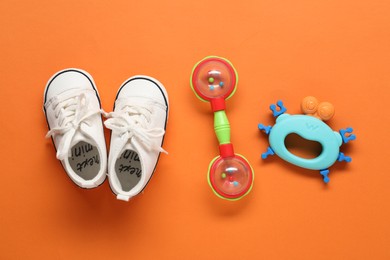 Baby rattles and booties on orange background, flat lay