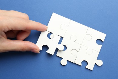 Woman solving white puzzle on blue background, top view