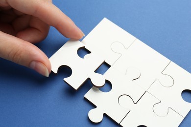 Photo of Woman solving white puzzle on blue background, closeup