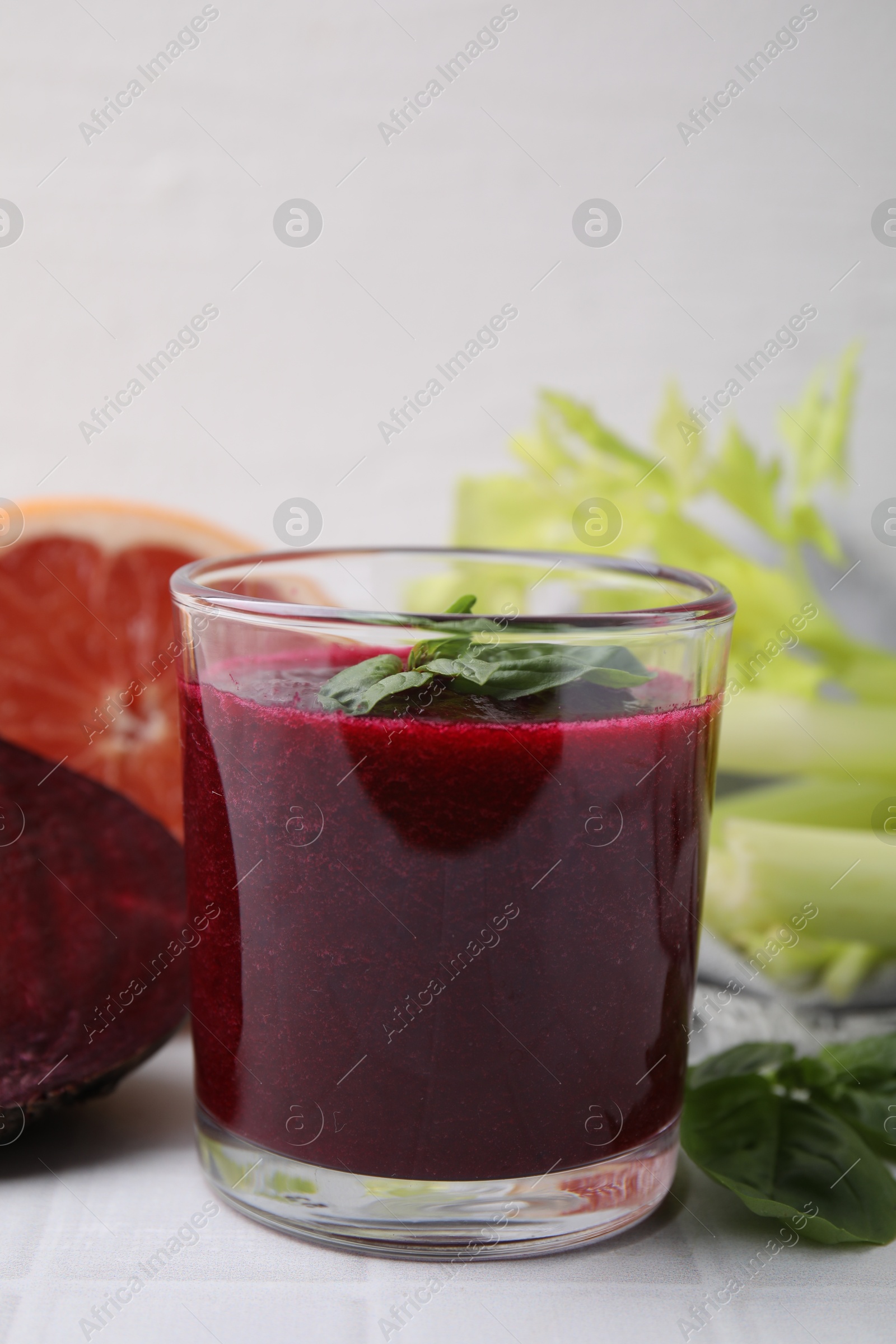 Photo of Tasty beetroot smoothie with basil in glass, fresh vegetables and grapefruit on light tiled table, closeup. Vegan drink