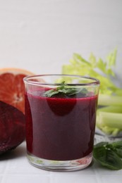 Photo of Tasty beetroot smoothie with basil in glass, fresh vegetables and grapefruit on light tiled table, closeup. Vegan drink