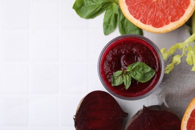 Photo of Tasty beetroot smoothie in glass, fresh vegetables, grapefruit and basil on white tiled table, flat lay with space for text. Vegan drink