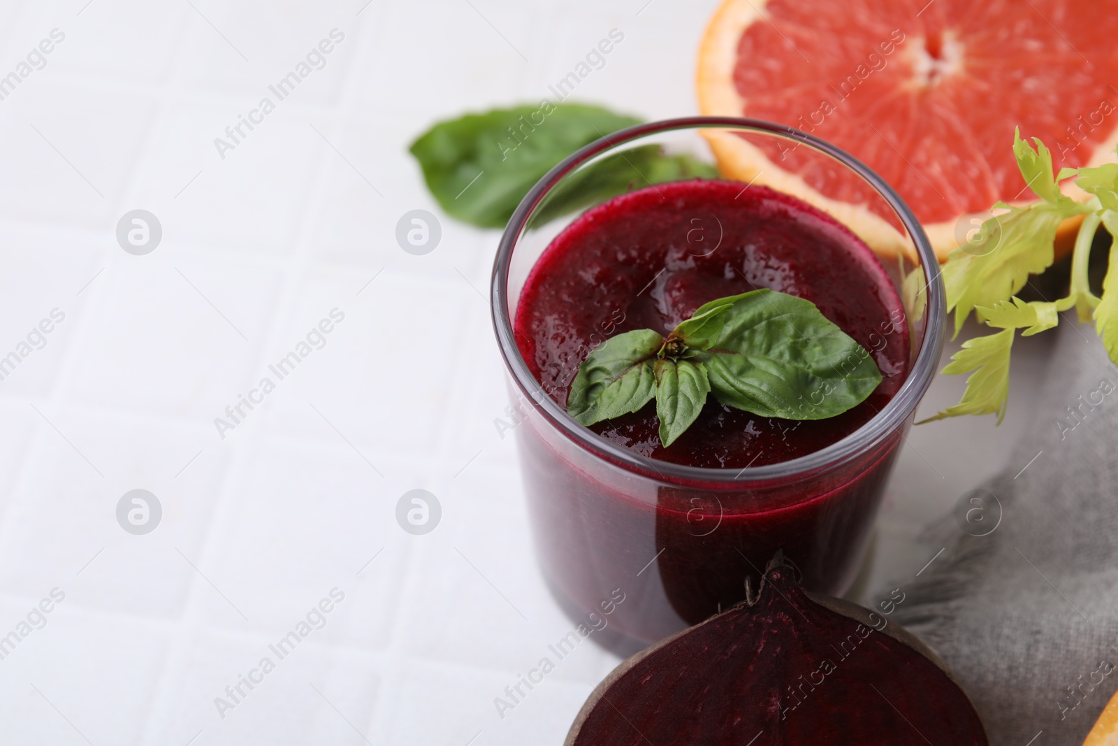 Photo of Vegan drink. Tasty beetroot smoothie in glass, fresh vegetables, grapefruit and basil on white tiled table, closeup. Space for text