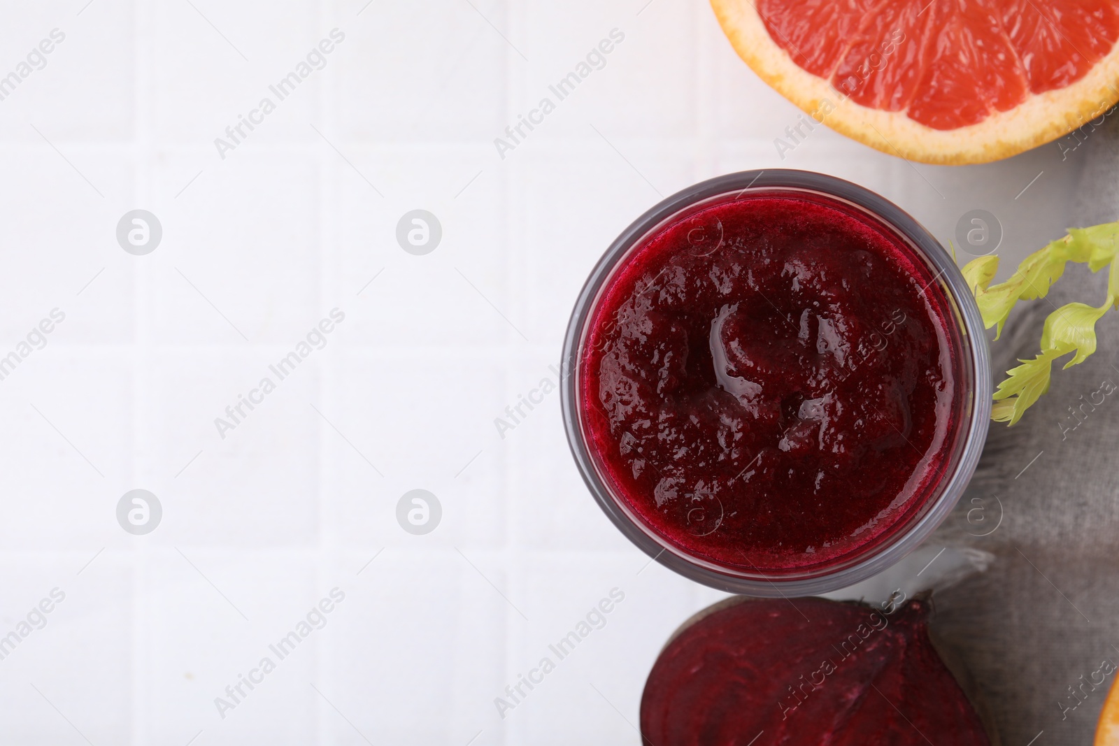 Photo of Tasty beetroot smoothie in glass, fresh vegetable and grapefruit on white tiled table, flat lay with space for text. Vegan drink