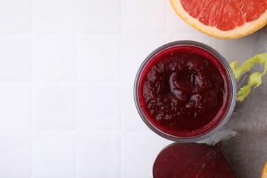 Photo of Tasty beetroot smoothie in glass, fresh vegetable and grapefruit on white tiled table, flat lay with space for text. Vegan drink