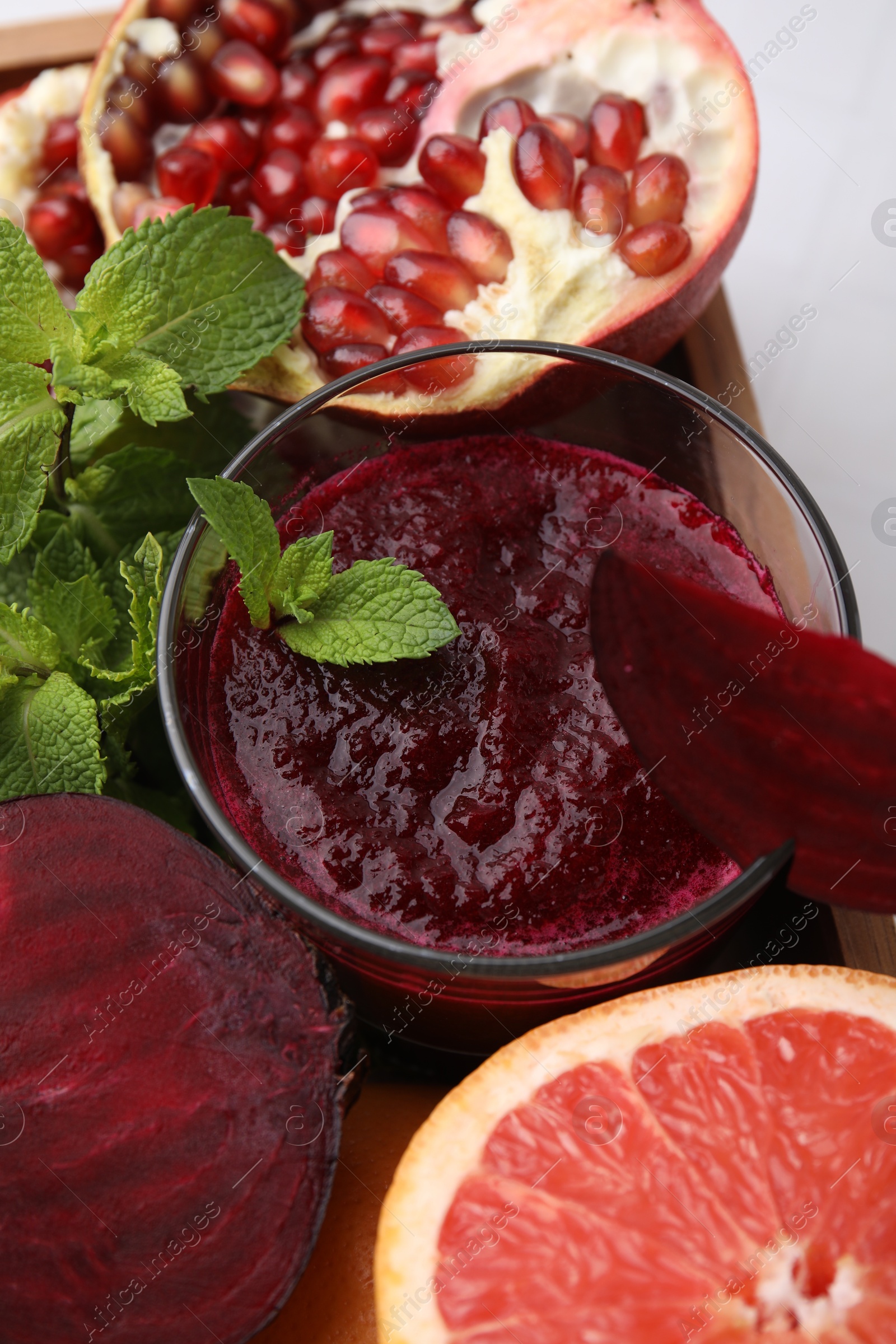 Photo of Tasty beetroot smoothie with mint in glass, fresh vegetables and fruits on table, closeup. Vegan drink