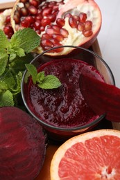 Photo of Tasty beetroot smoothie with mint in glass, fresh vegetables and fruits on table, closeup. Vegan drink