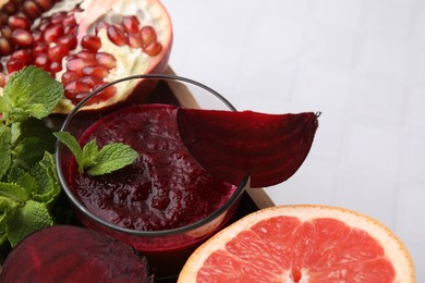 Tasty beetroot smoothie with mint in glass, fresh vegetables and fruits on white table, closeup. Vegan drink