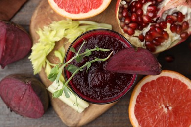 Photo of Tasty beetroot smoothie with microgreens in glass, fresh vegetables and fruits on wooden table, top view. Vegan drink