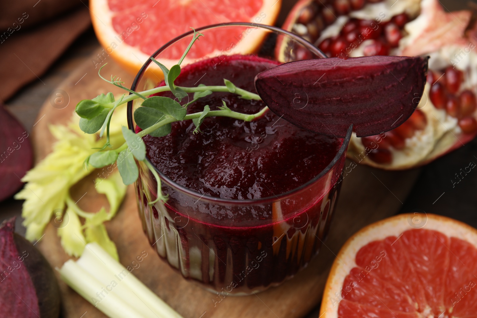 Photo of Tasty beetroot smoothie with microgreens in glass, fresh vegetables and fruits on wooden table, closeup. Vegan drink