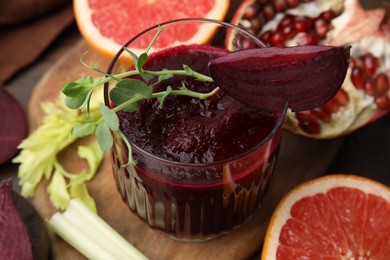 Photo of Tasty beetroot smoothie with microgreens in glass, fresh vegetables and fruits on wooden table, closeup. Vegan drink