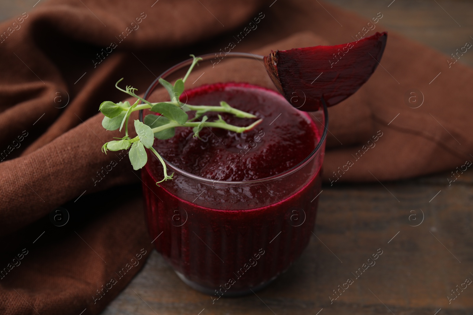 Photo of Tasty beetroot smoothie with microgreens in glass on wooden table, closeup. Vegan drink