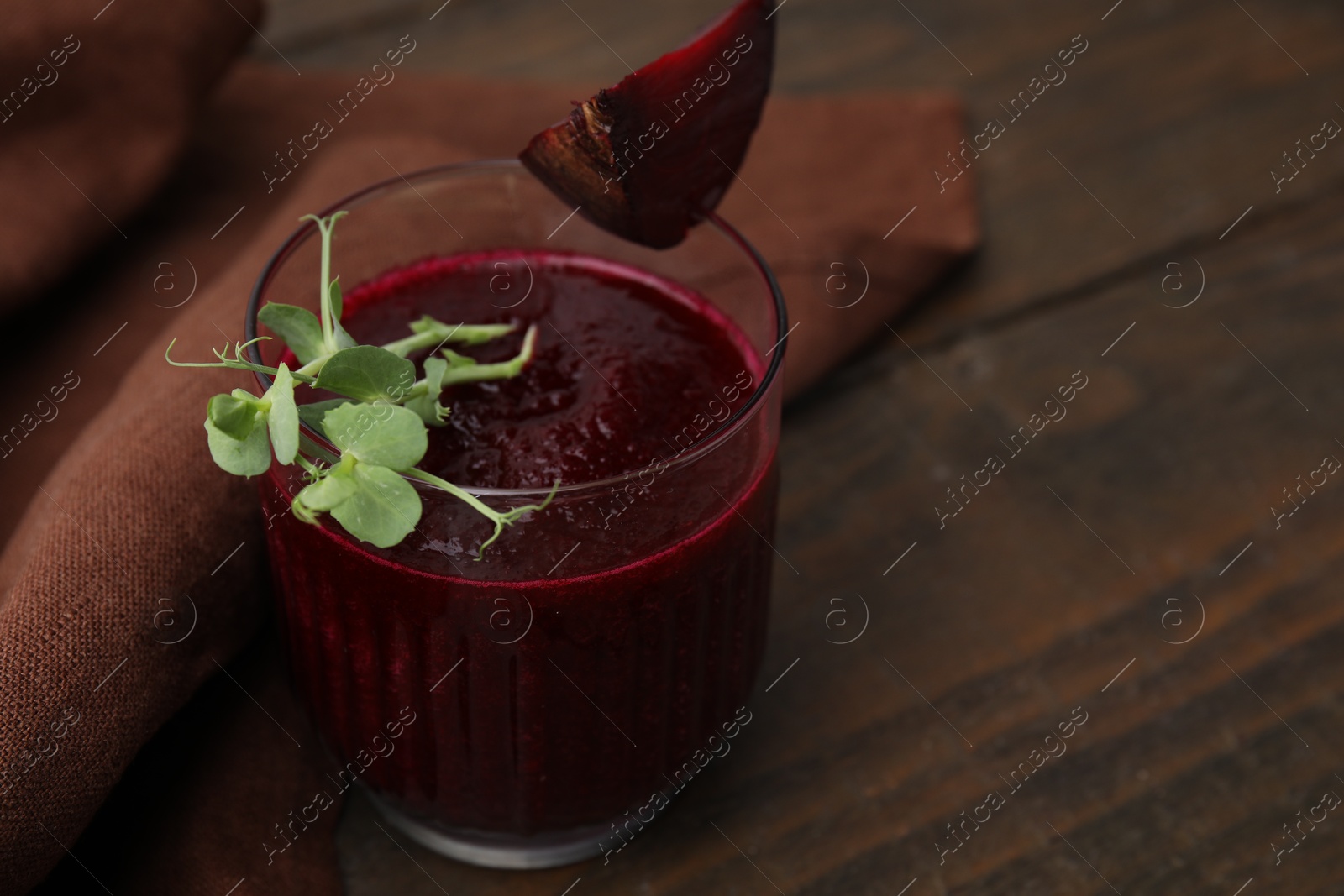 Photo of Vegan drink. Tasty beetroot smoothie with microgreens in glass on wooden table, closeup. Space for text