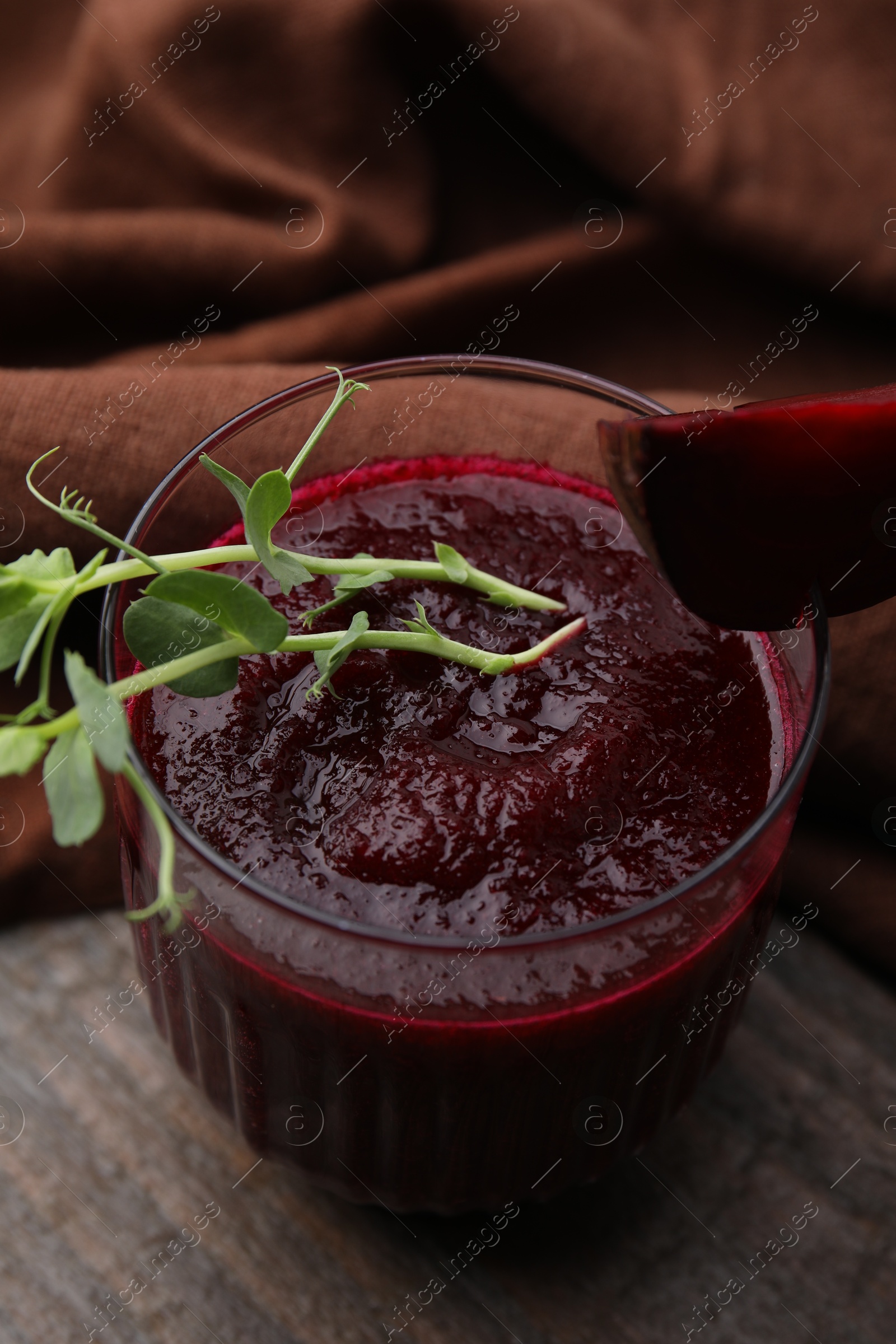 Photo of Tasty beetroot smoothie with microgreens in glass on wooden table, closeup. Vegan drink