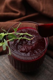 Photo of Tasty beetroot smoothie with microgreens in glass on wooden table, closeup. Vegan drink