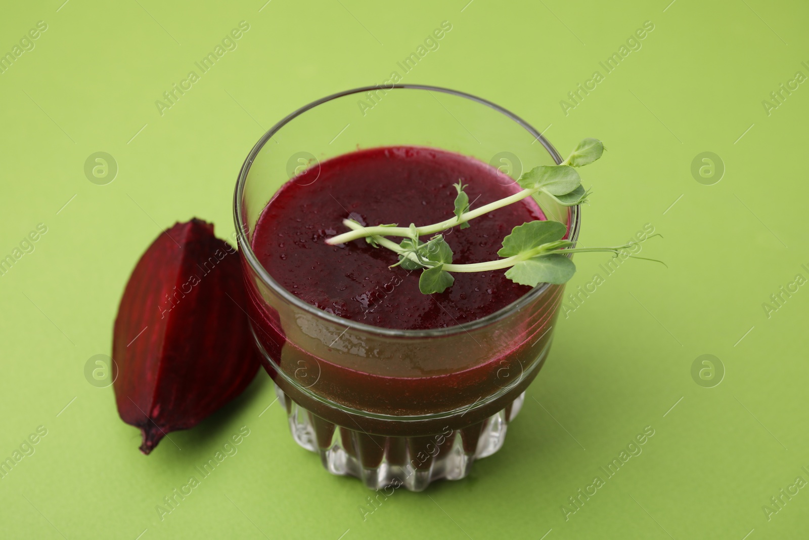 Photo of Tasty beetroot smoothie with microgreens in glass on green table, closeup. Vegan drink