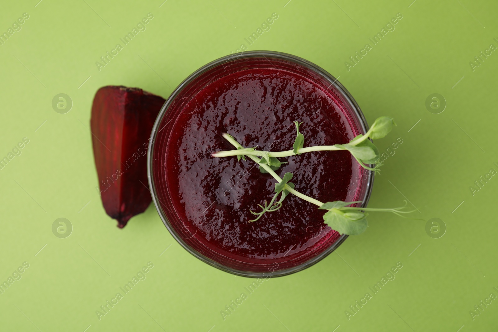 Photo of Tasty beetroot smoothie with microgreens in glass on green table, top view. Vegan drink