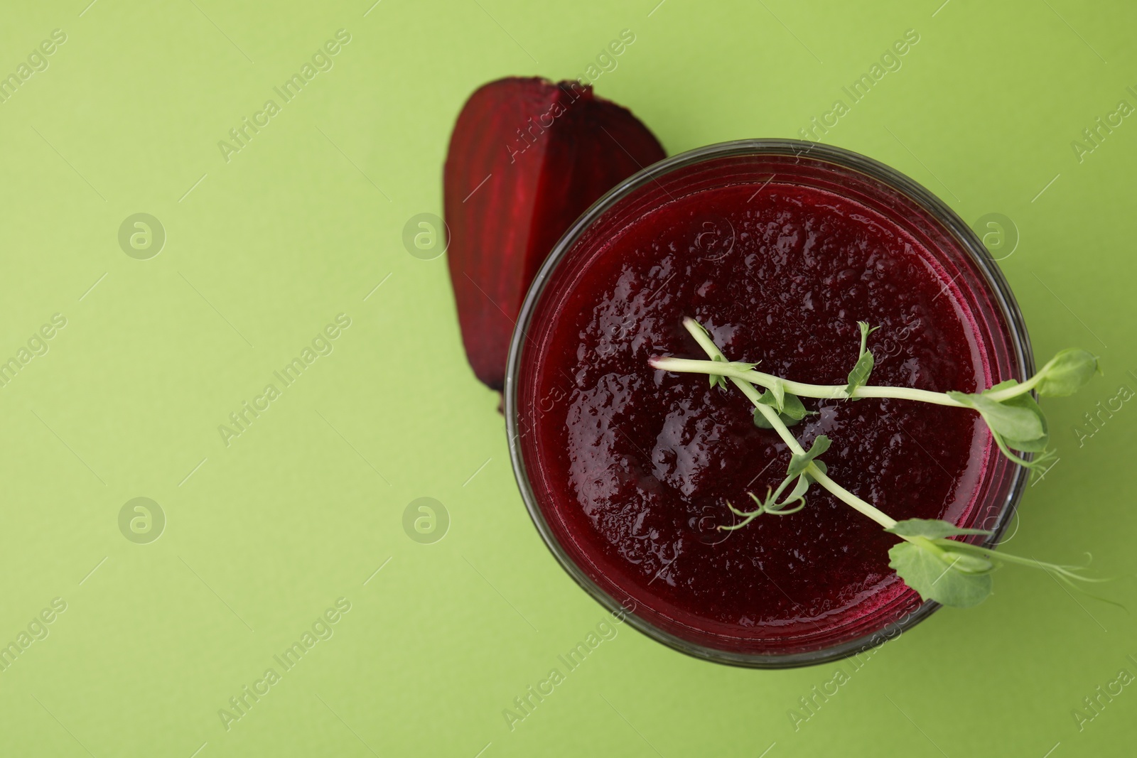 Photo of Tasty beetroot smoothie with microgreens in glass on green table, top view and space for text. Vegan drink