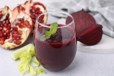Photo of Tasty beetroot smoothie with mint in glass, fresh vegetables and pomegranate on light table, closeup. Vegan drink