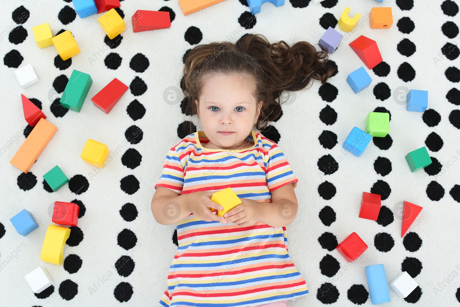 Photo of Cute little girl and toys on floor, top view