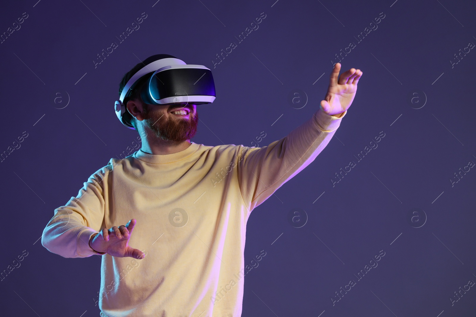 Photo of Smiling man using virtual reality headset on dark purple background. Space for text