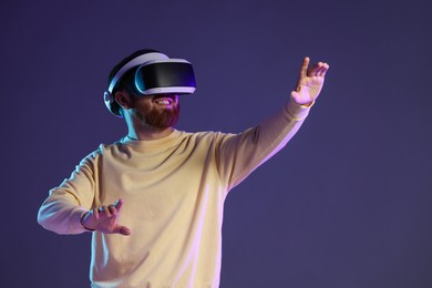 Smiling man using virtual reality headset on dark purple background. Space for text