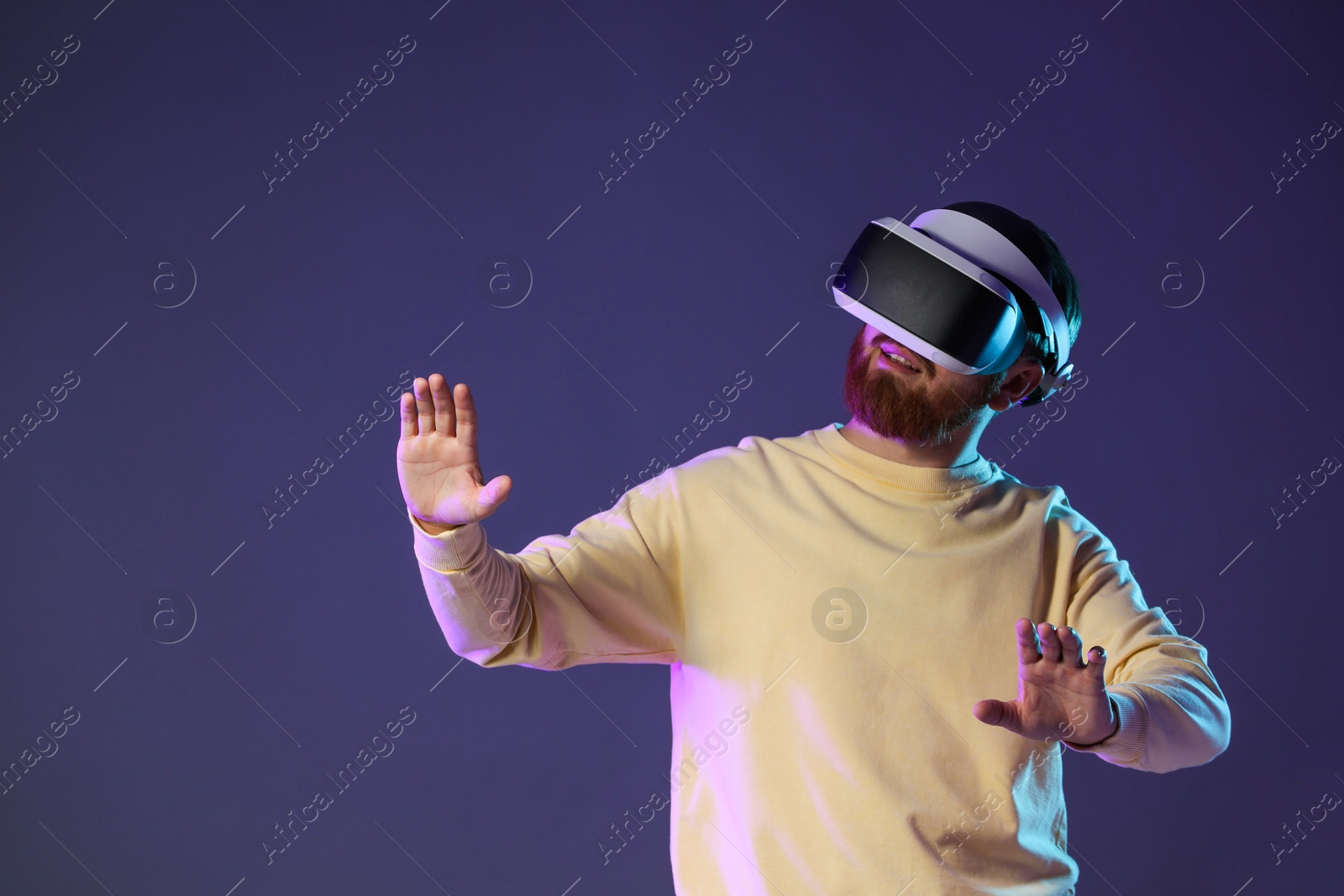 Photo of Man using virtual reality headset on dark purple background. Space for text