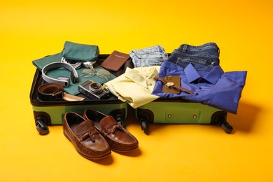 Photo of Open suitcase with traveler's belongings on yellow background