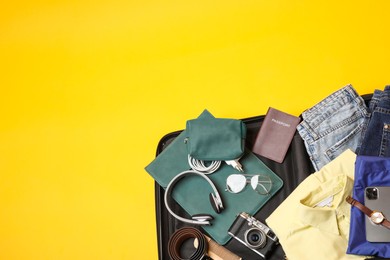 Open suitcase with traveler's belongings on yellow background, top view. Space for text