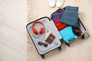 Open suitcase with traveler's belongings on floor, flat lay. Space for text