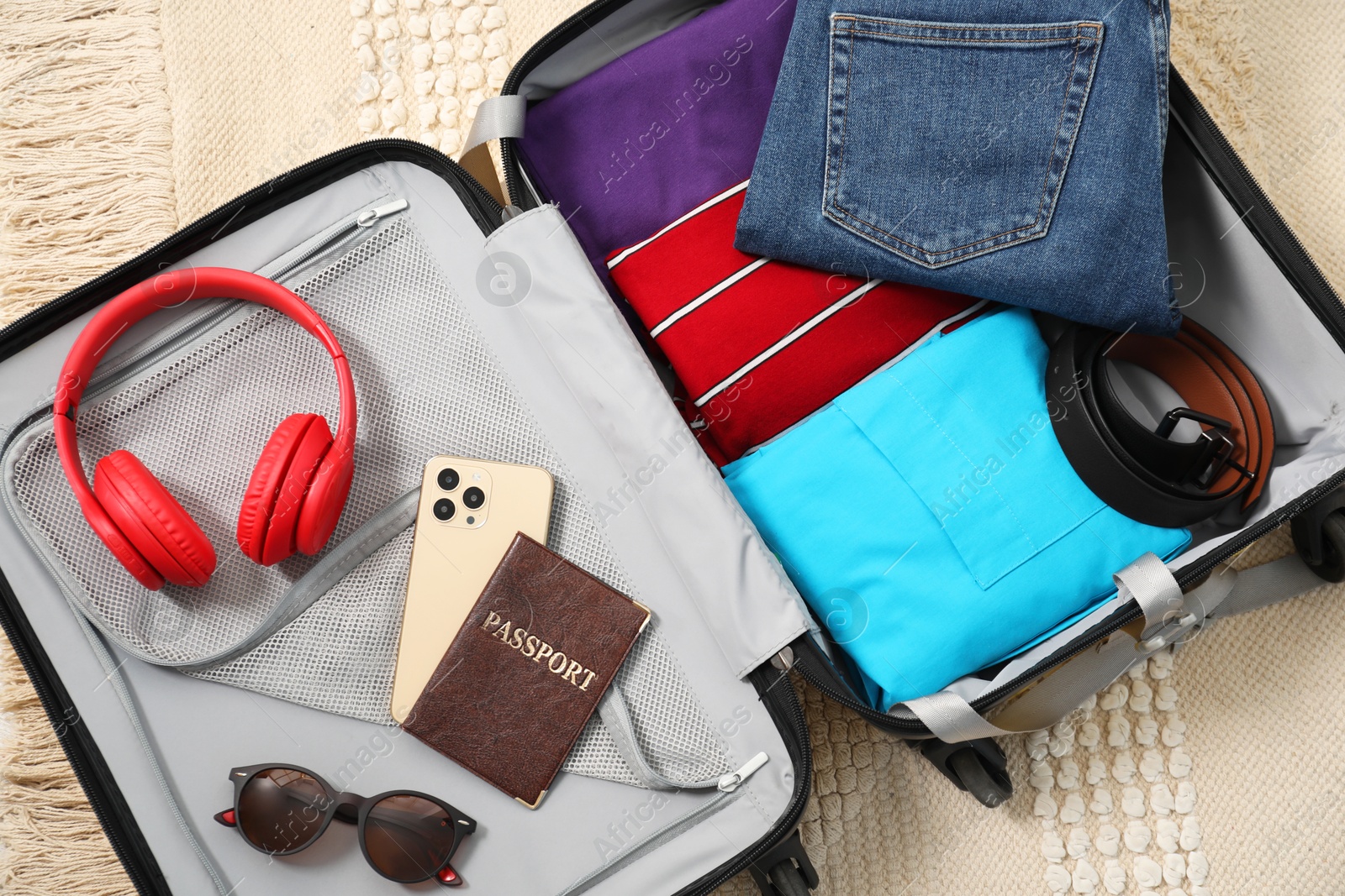 Photo of Open suitcase with traveler's belongings on floor, top view