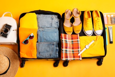 Photo of Open suitcase with traveler's belongings on yellow background, flat lay