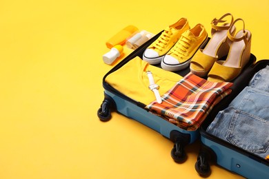 Open suitcase with traveler's belongings on yellow background, space for text