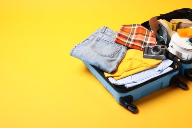 Open suitcase with traveler's belongings on yellow background, space for text