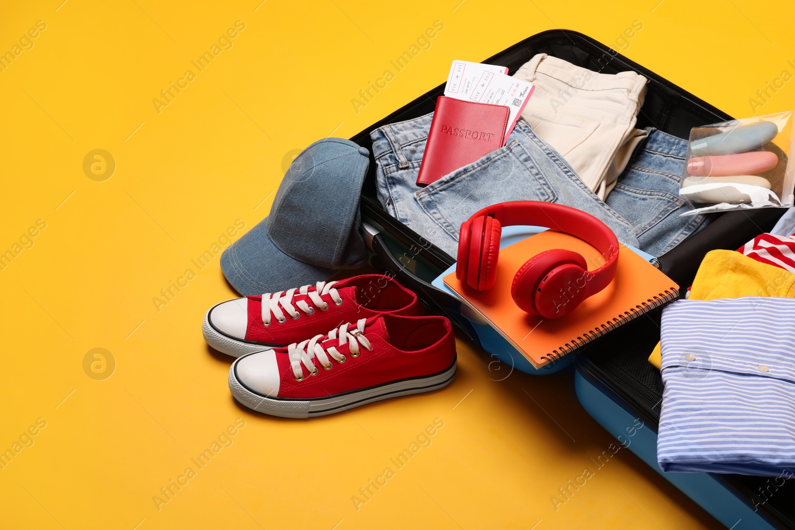 Photo of Open suitcase with traveler's belongings on yellow background, space for text